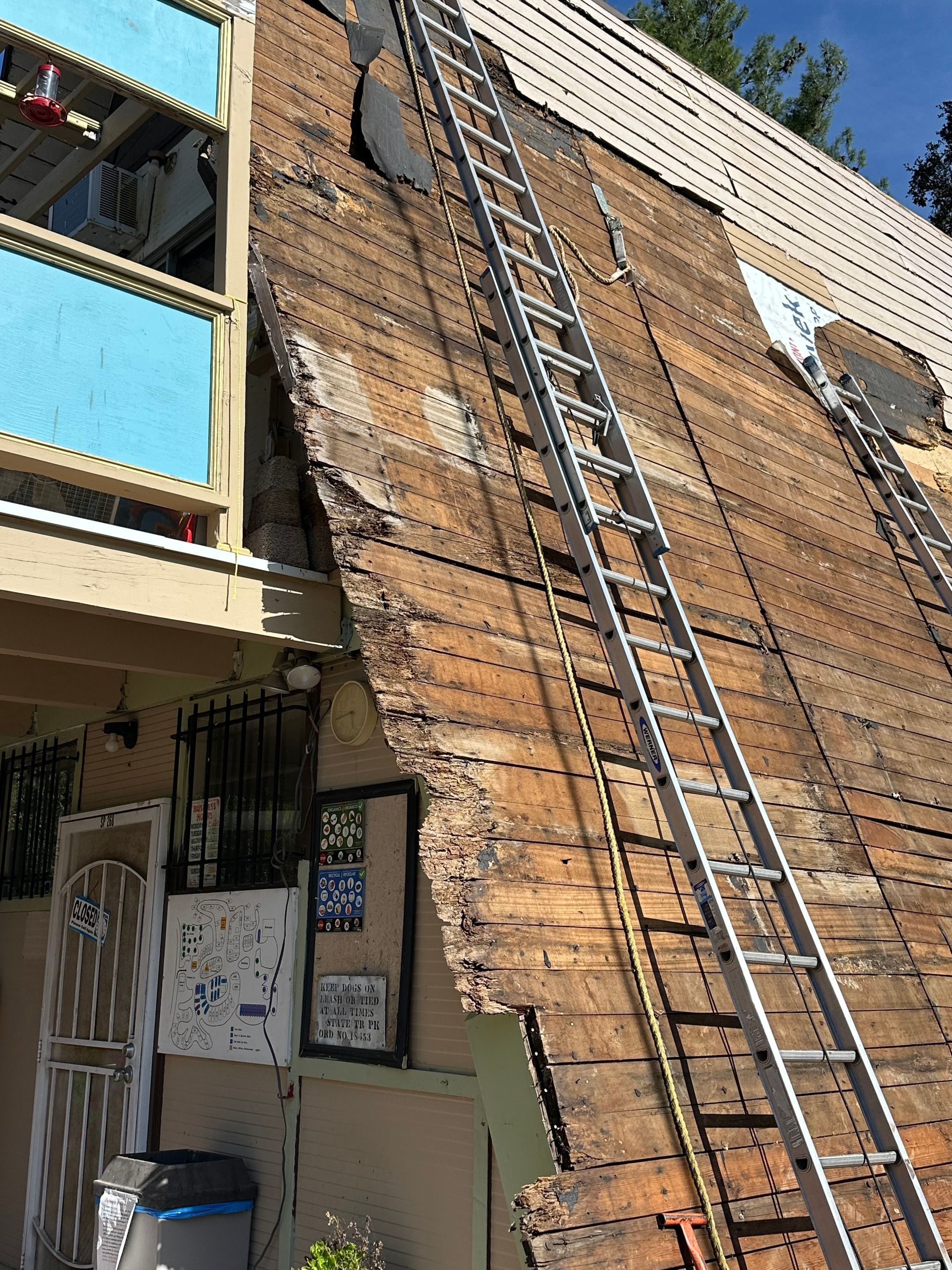 Building exterior with damaged siding and two ladders leaning against the structure.
