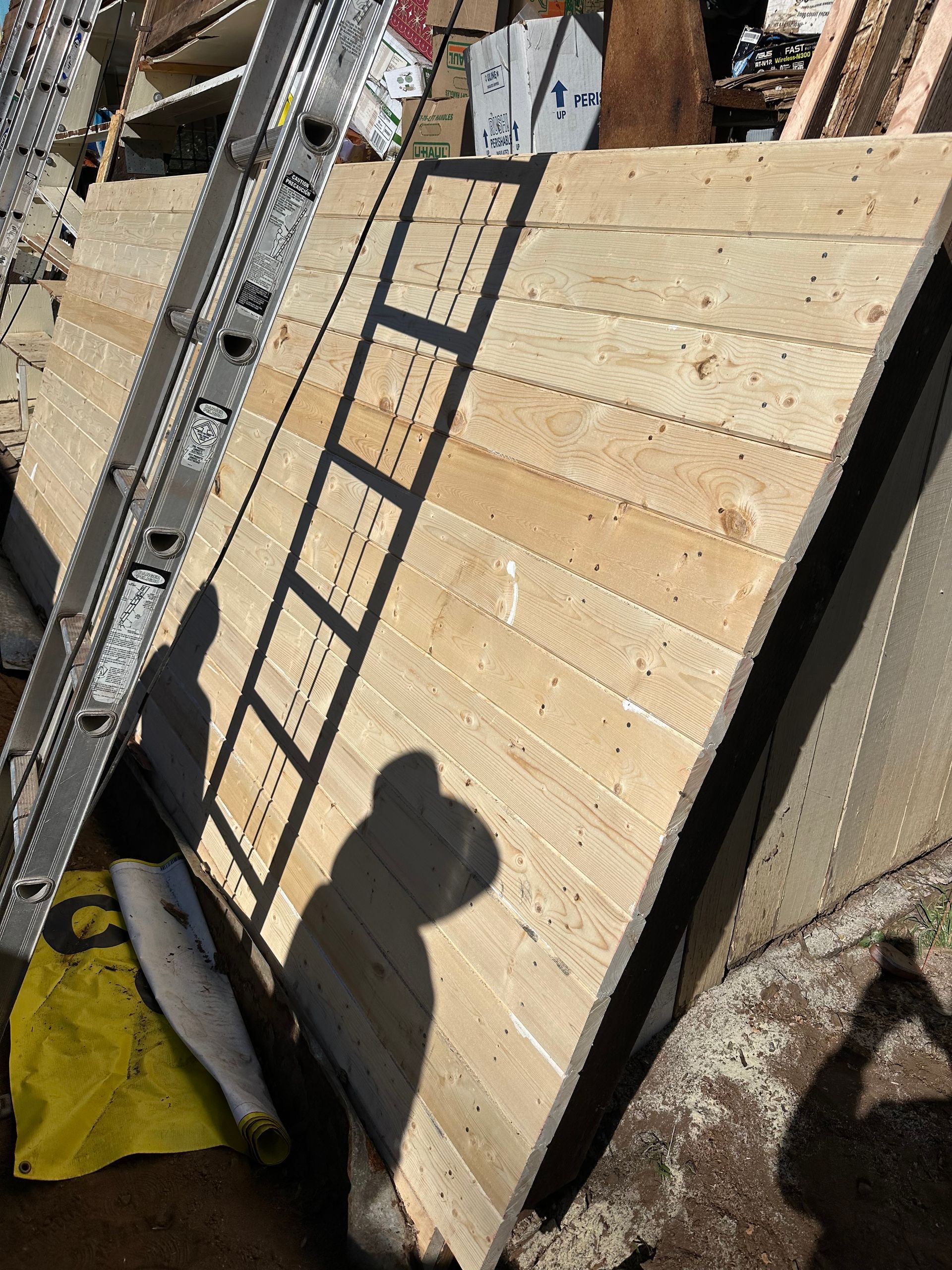 Large wooden panel with ladder leaning against it, casting a shadow.