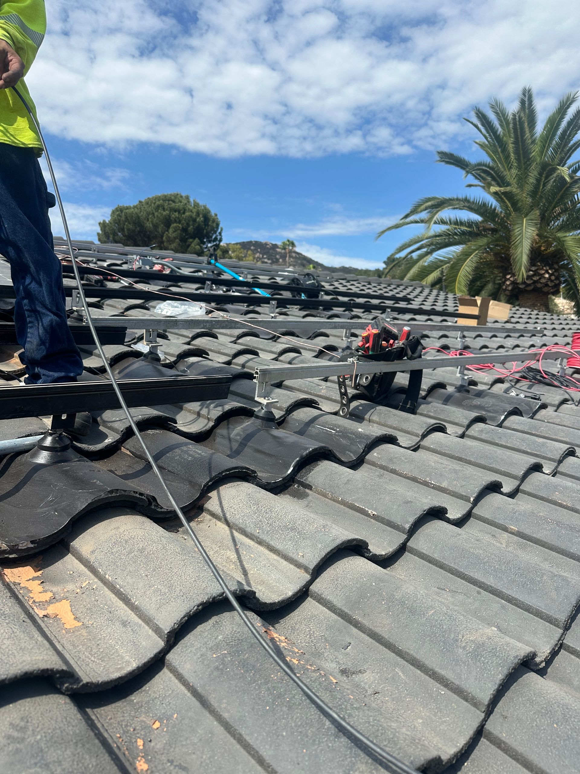 Roof workers installing dark tiles on a house roof under a blue sky with palm trees nearby