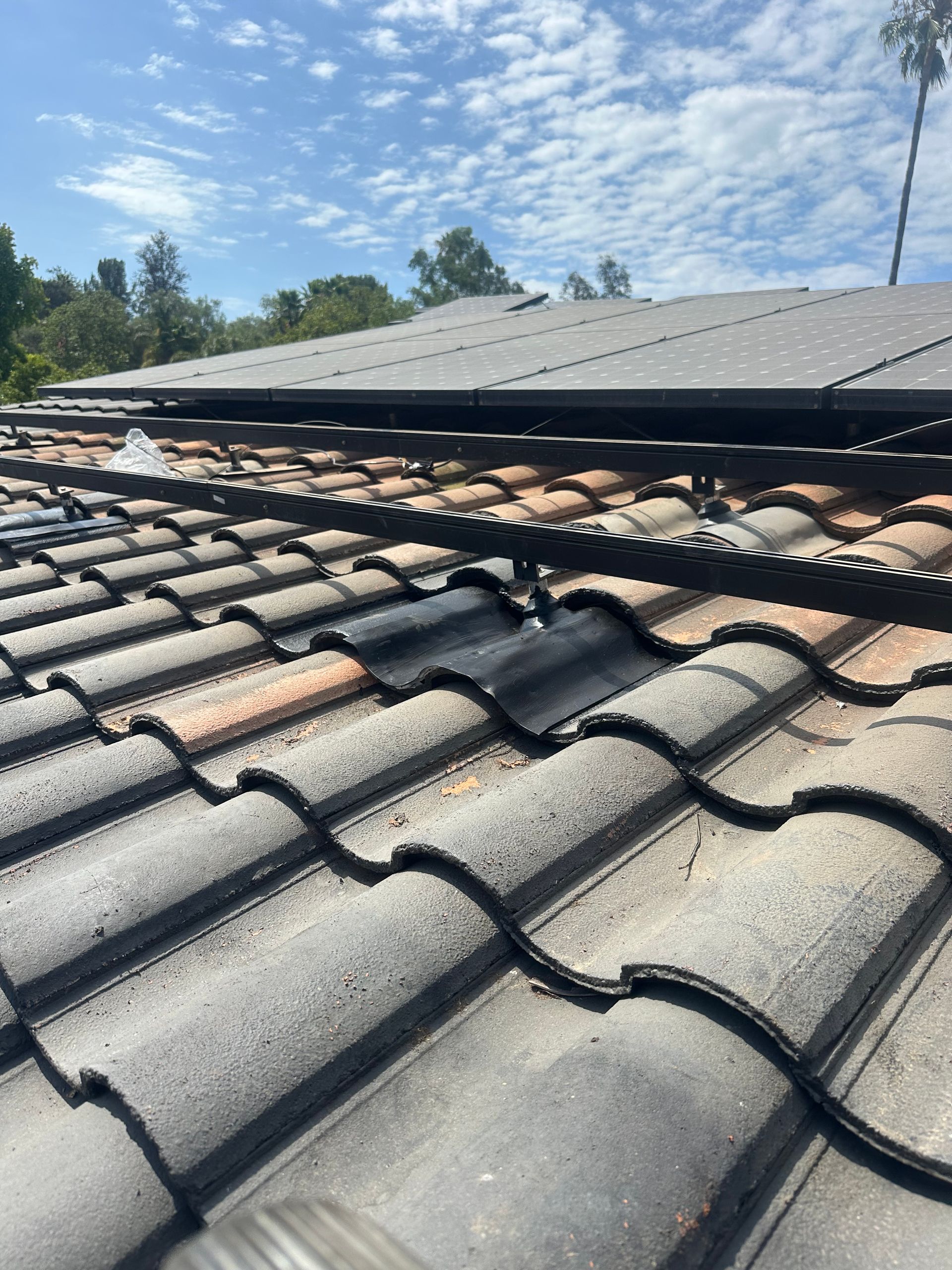 Damaged clay-tile roof with lifted shingles beneath a solar panel array under a blue sky
