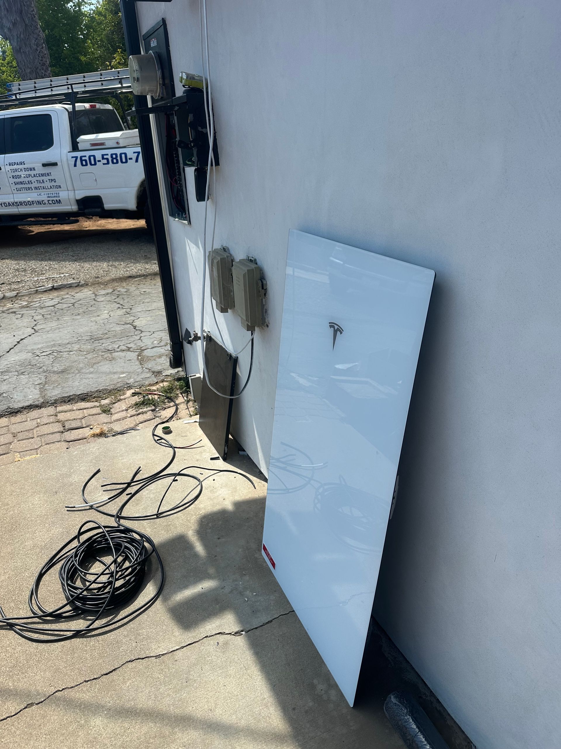 White panel leaning against a building wall beside a coiled cable and parked utility truck