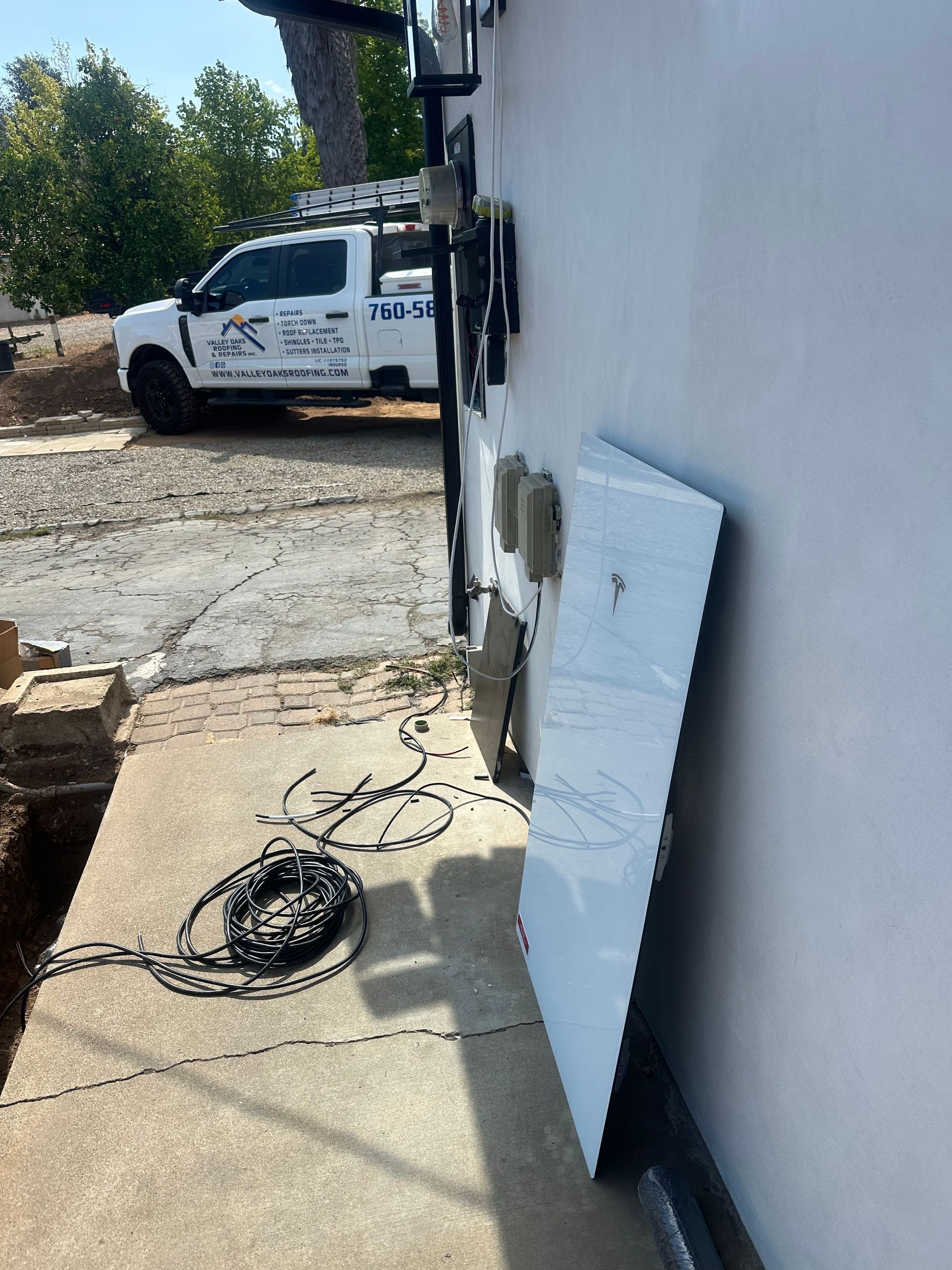 White truck parked outside a building beside coiled cables and a leaning white panel on a sunlit sidewalk