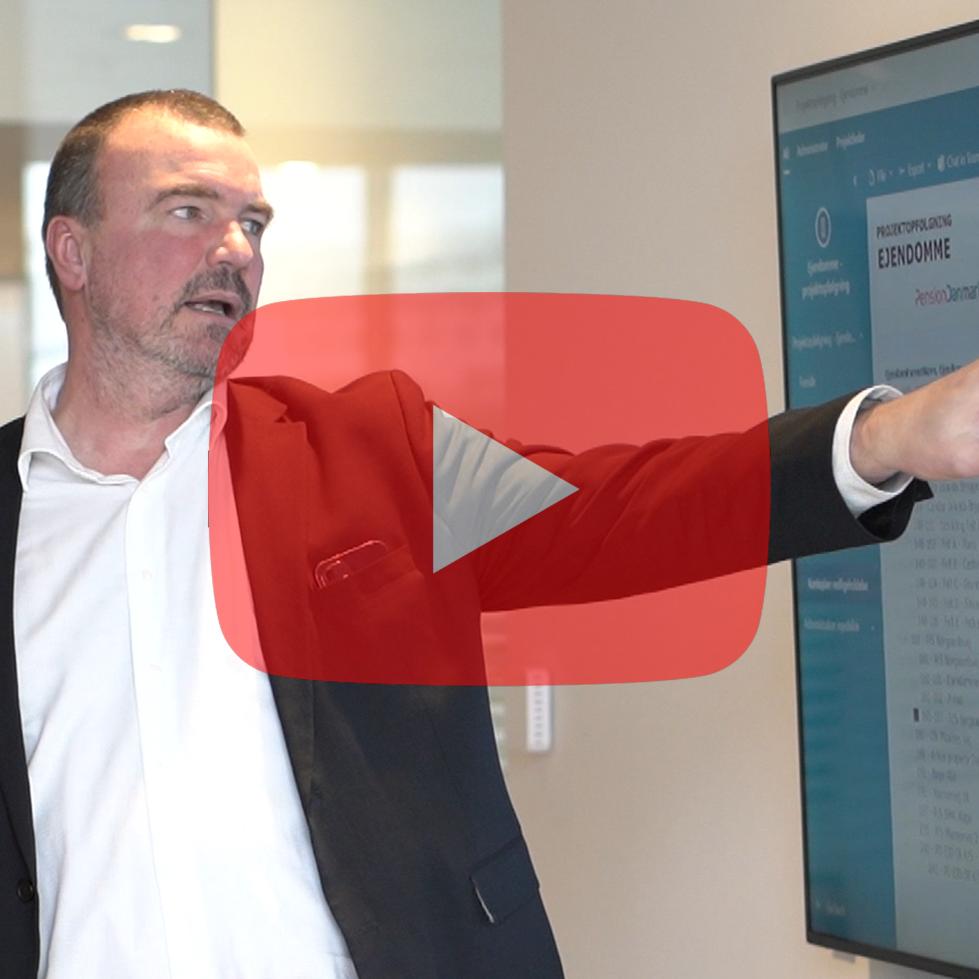 En mand i jakkesæt peger på en skærm med et youtube-logo i hjørnet