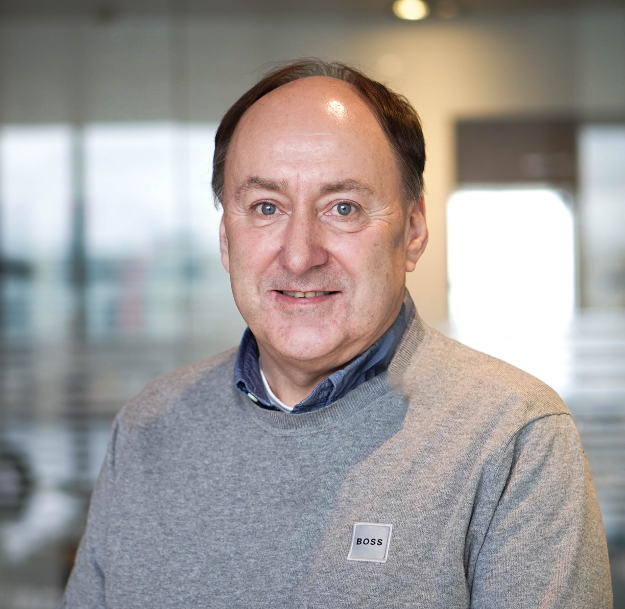 A man wearing a grey sweater and a blue shirt is smiling for the camera.