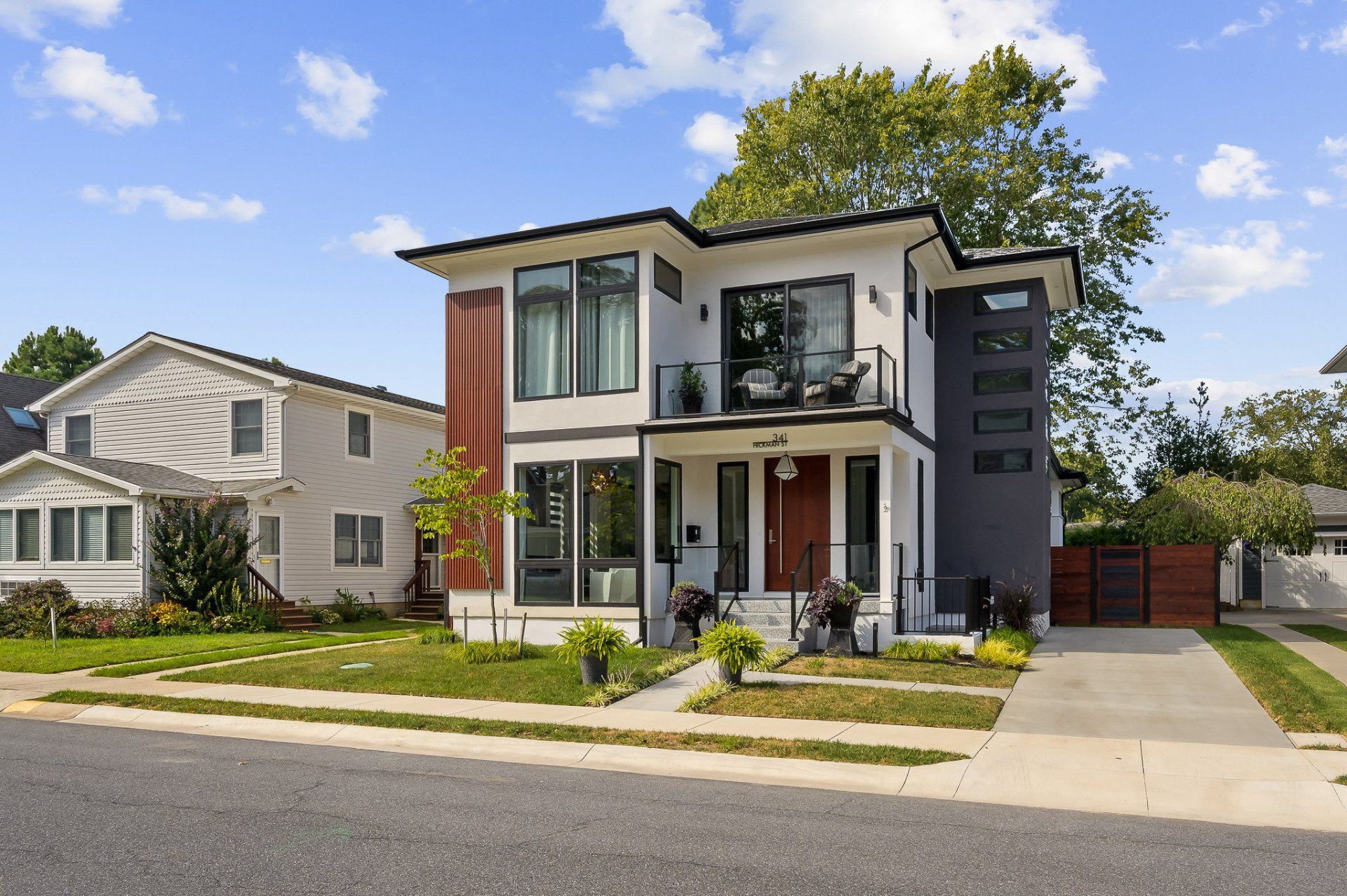 Modern two-story house with white, gray, and red accents; parked in front of a tree and grass.