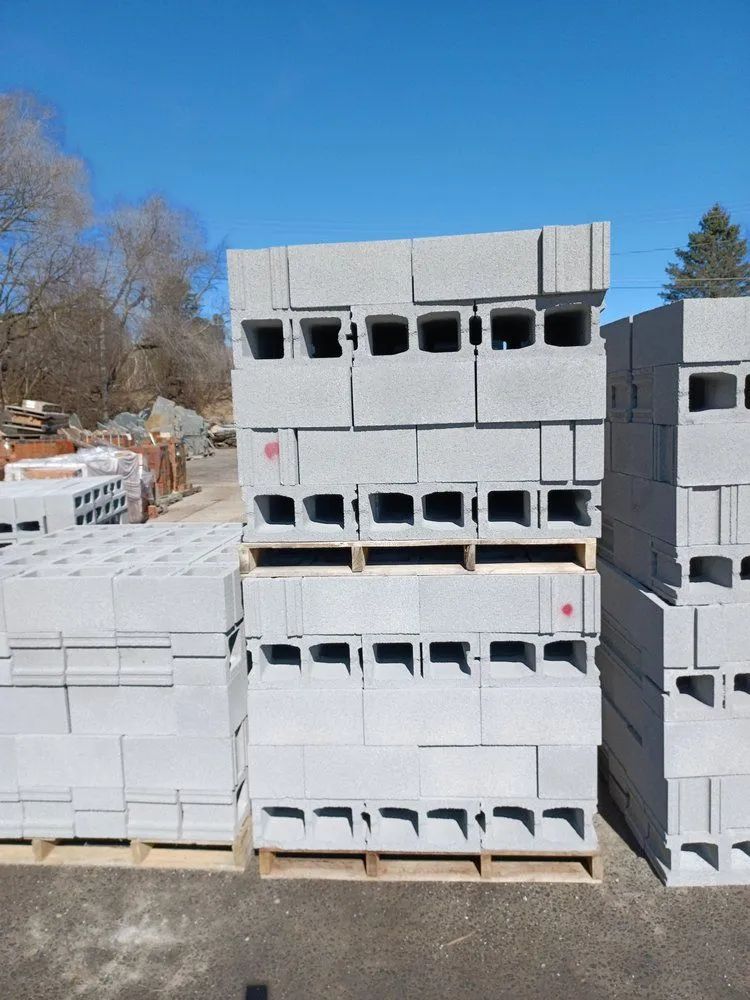 Stacks of gray concrete masonry blocks on wooden pallets outdoors under a clear blue sky.