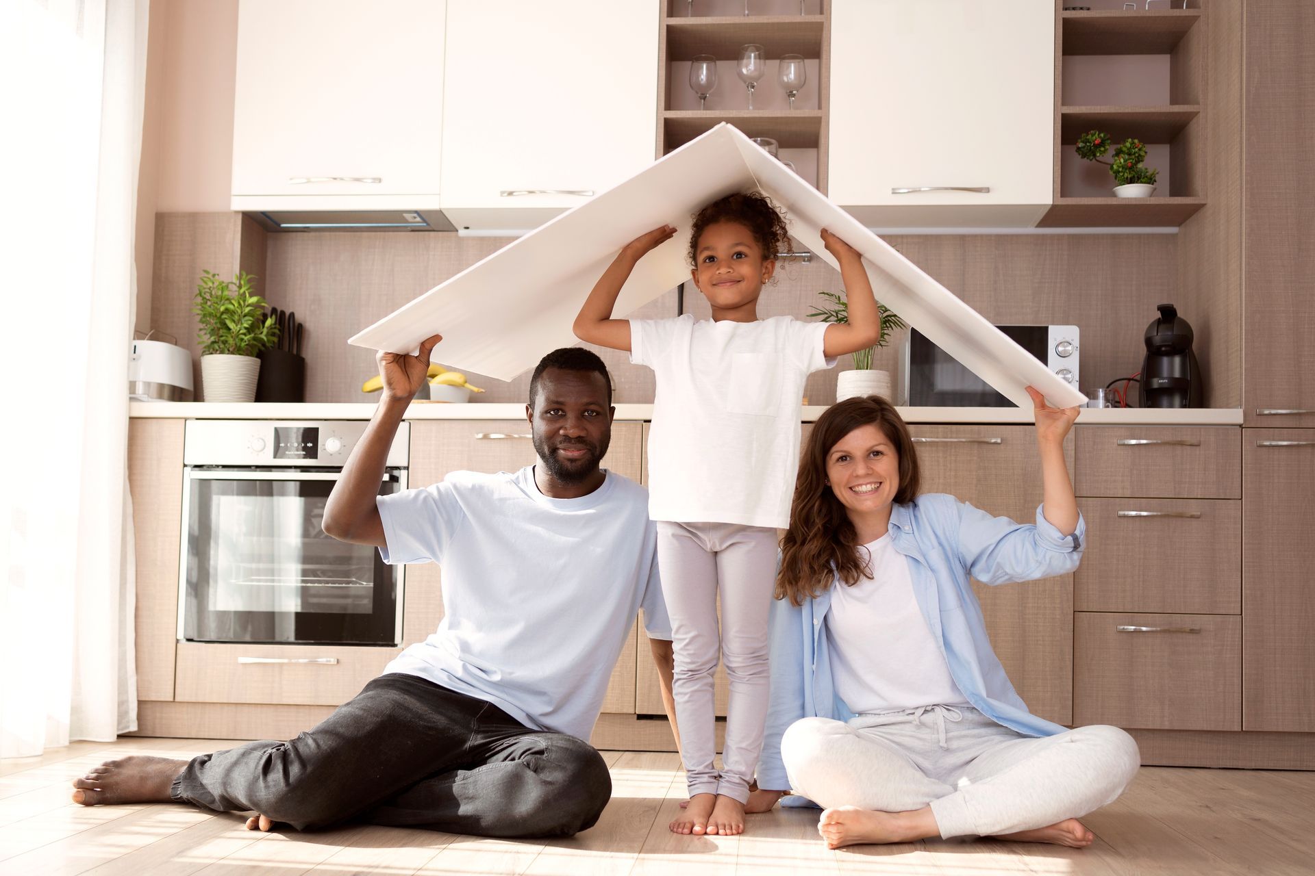 Uma família está sentada na cozinha, segurando um pedaço de papel em forma de telhado sobre suas cabeças.