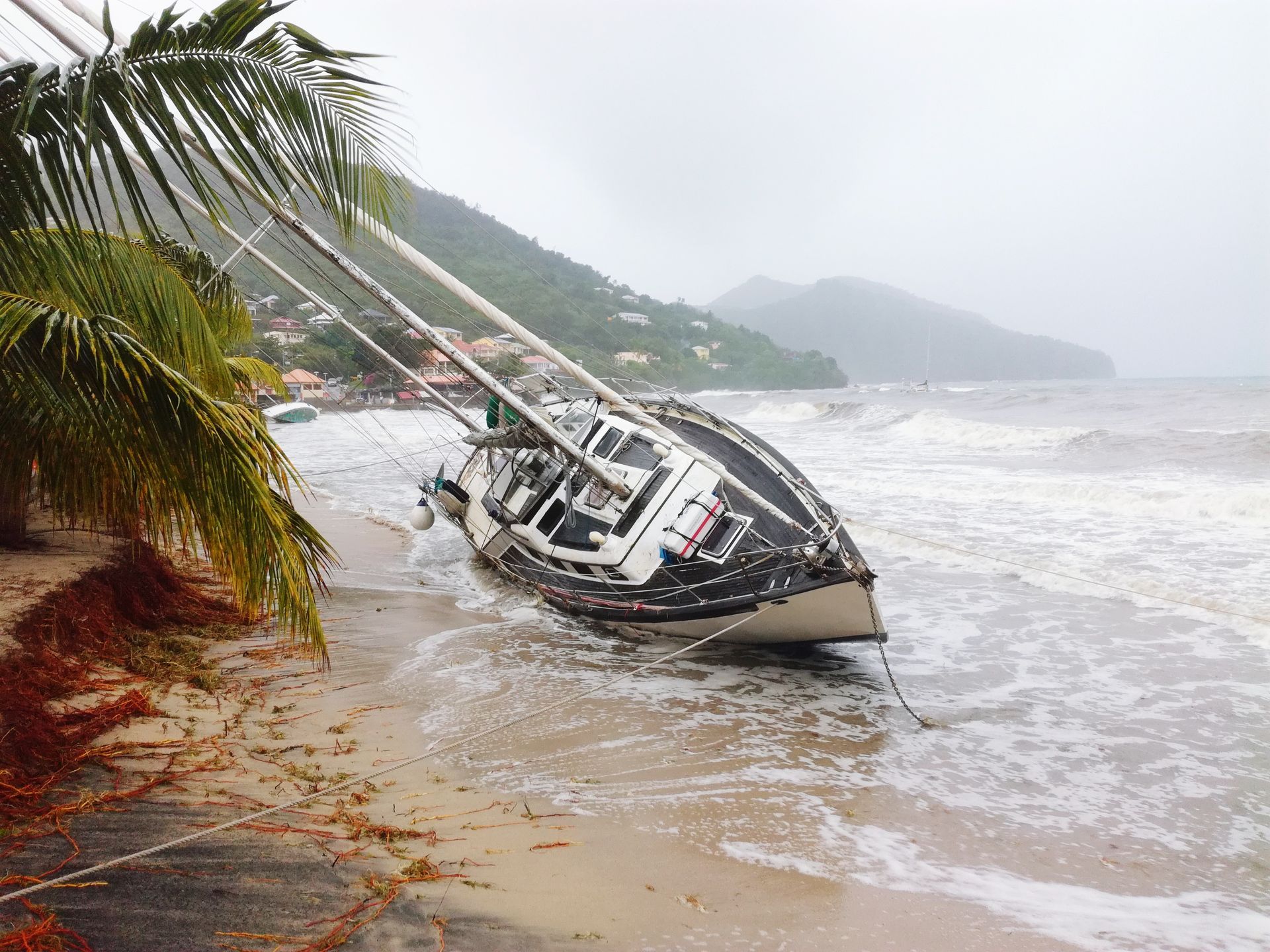 Veleiro danificado arrastado para uma praia arenosa durante uma tempestade, com ondas violentas quebrando contra seu casco.