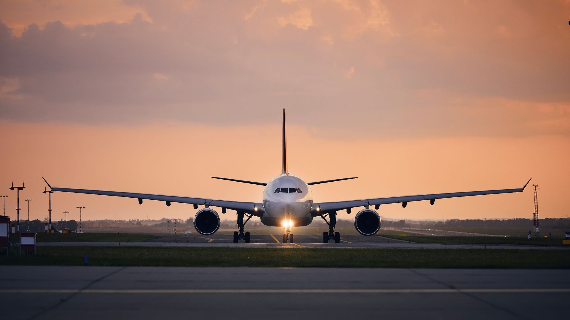 Um avião comercial visto de frente enquanto taxiava na pista de um aeroporto, contra um céu crepuscular com tons alaranjados.