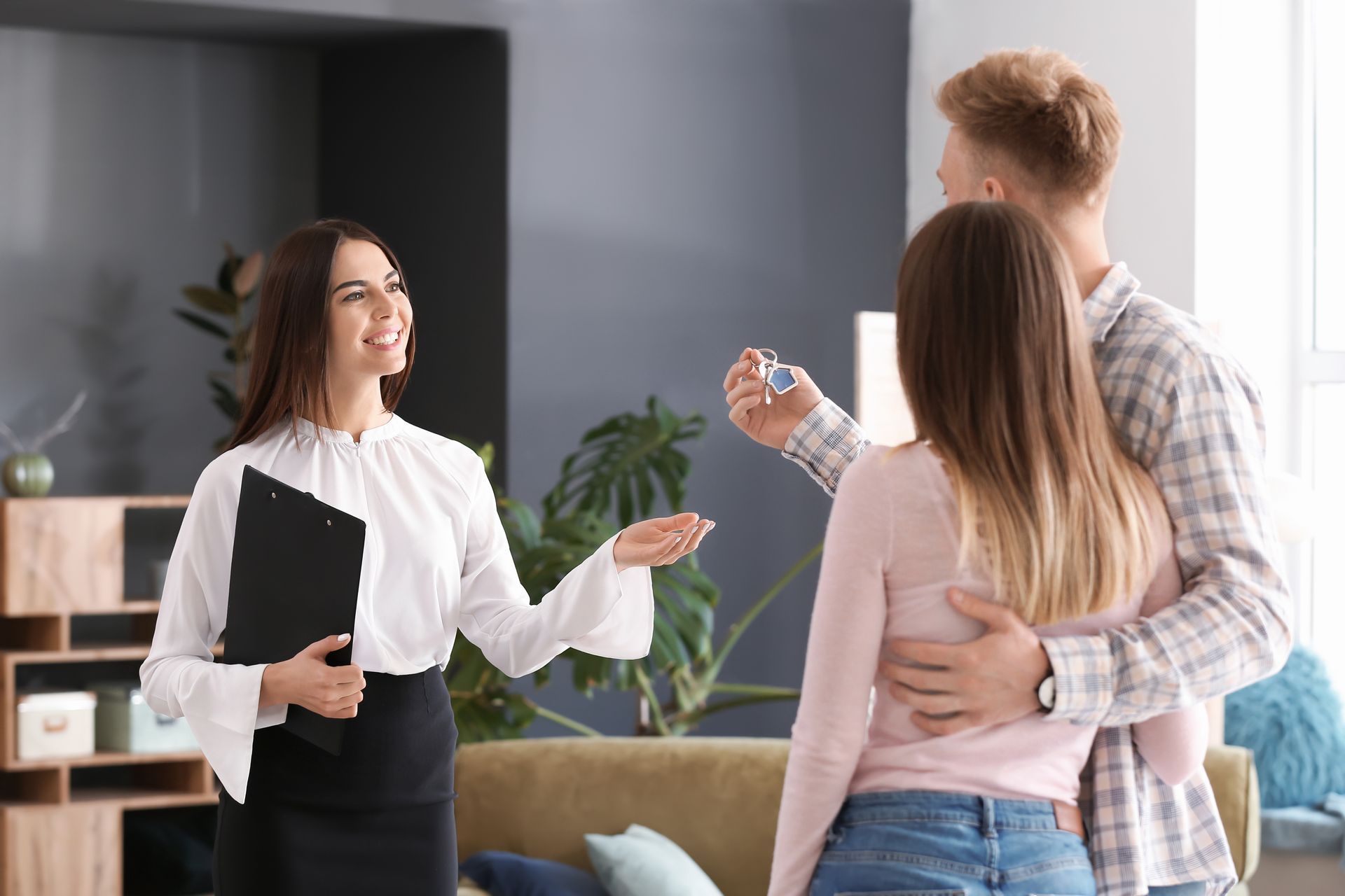 Two people chatting with a smiling woman holding a clipboard in a modern office lounge