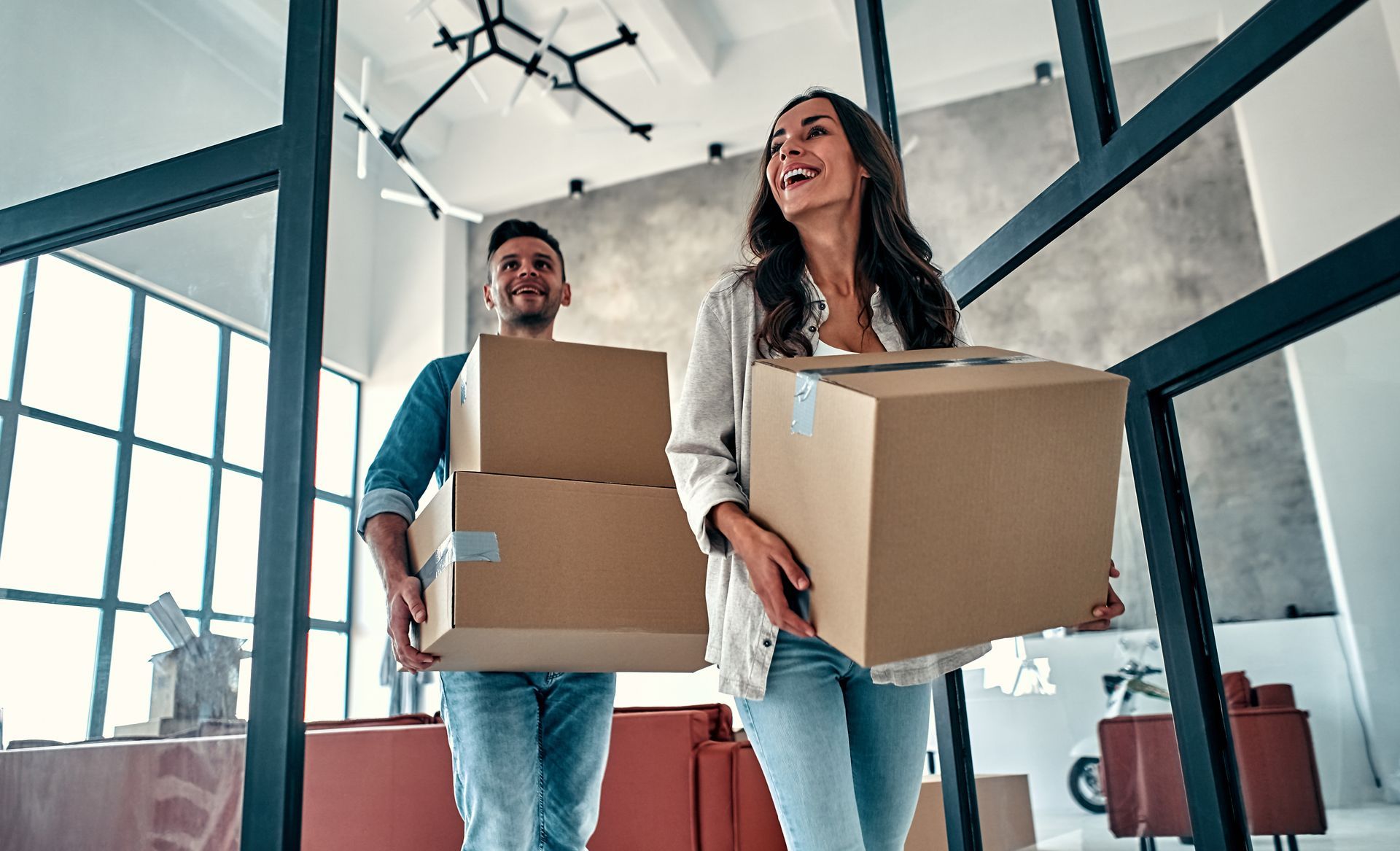 Two people carry cardboard boxes through a bright office space