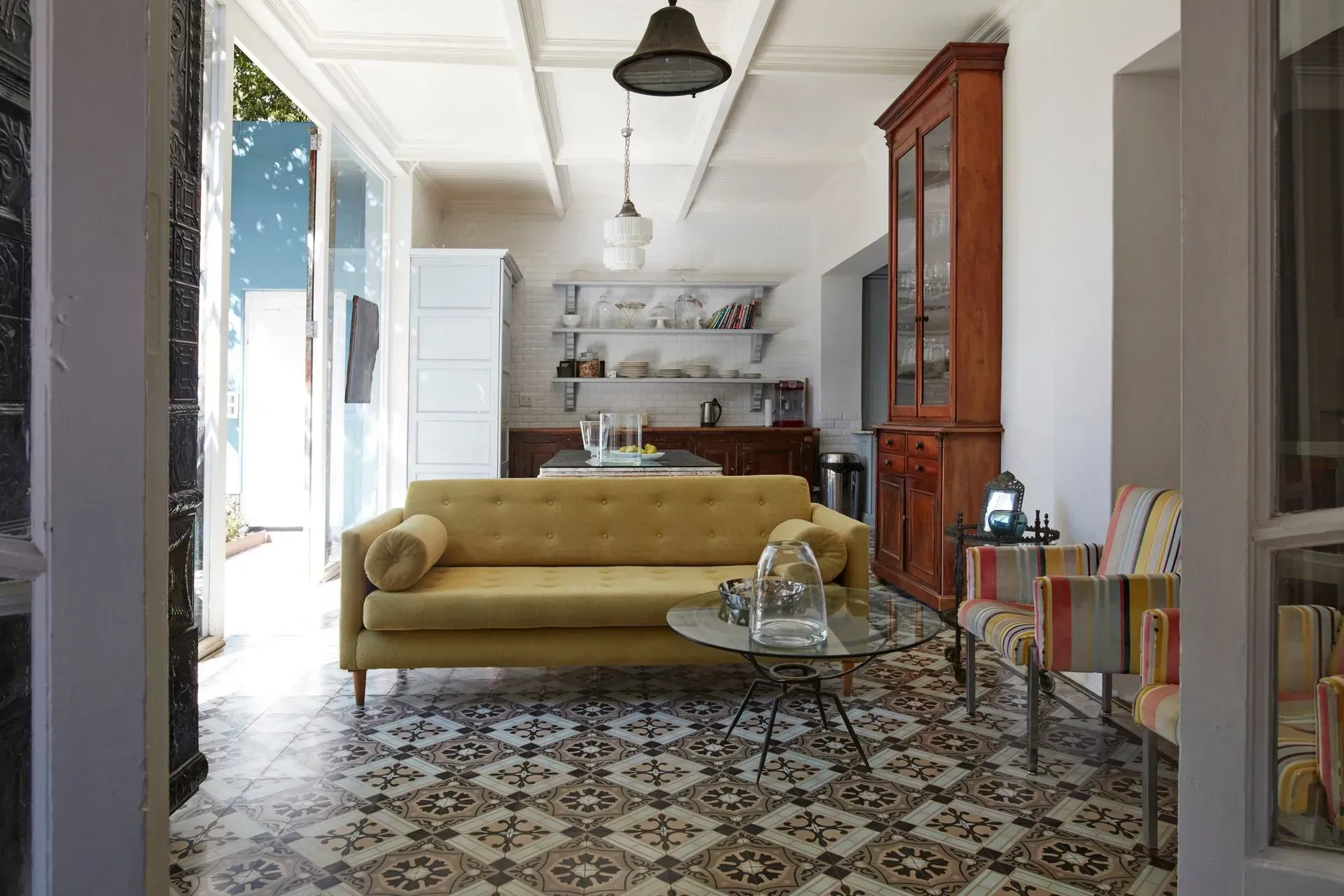 Bright living room with a yellow sofa, patterned tile floor, and open kitchen shelves in back
