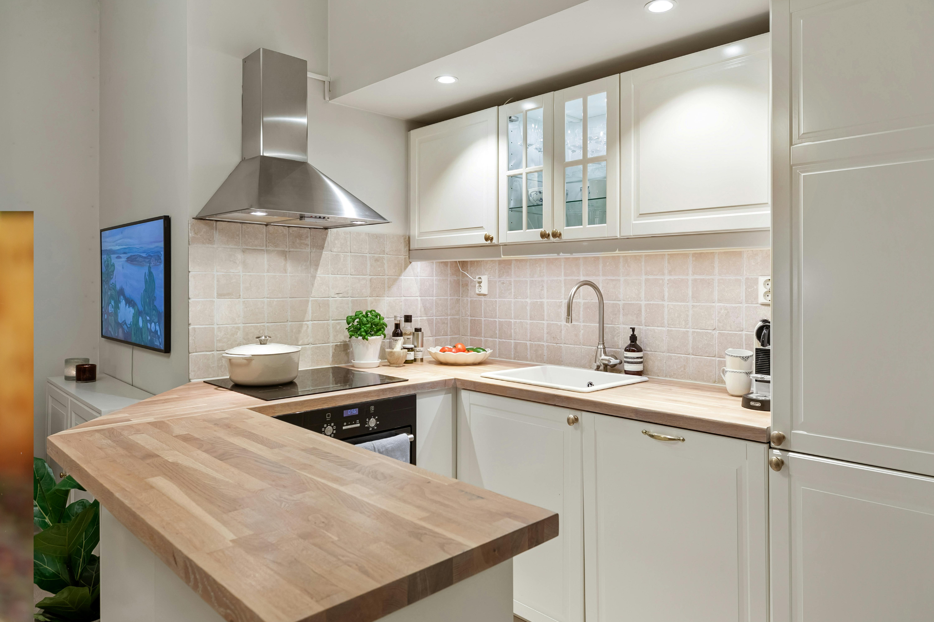 Modern white kitchen with wood island, stainless range hood, and beige tiled backsplash
