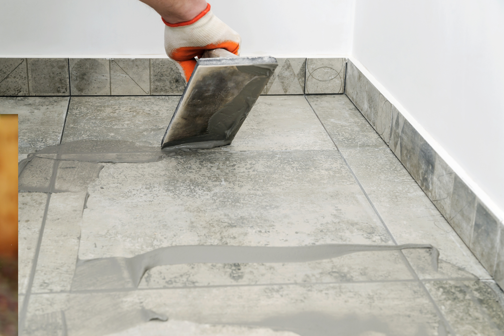 Hand gloved in orange holding a tile over a tiled floor during installation