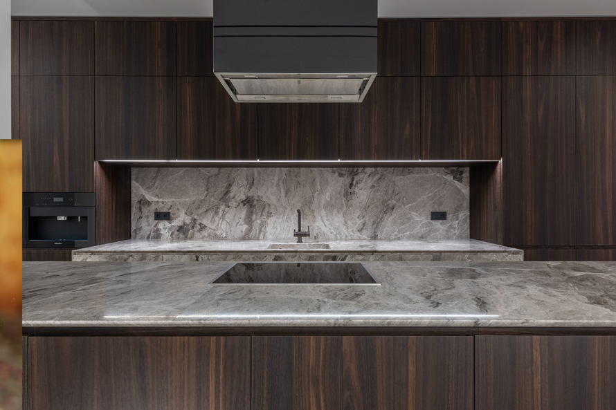 Modern kitchen with dark wood cabinets, gray stone countertops, and a stainless steel range hood.