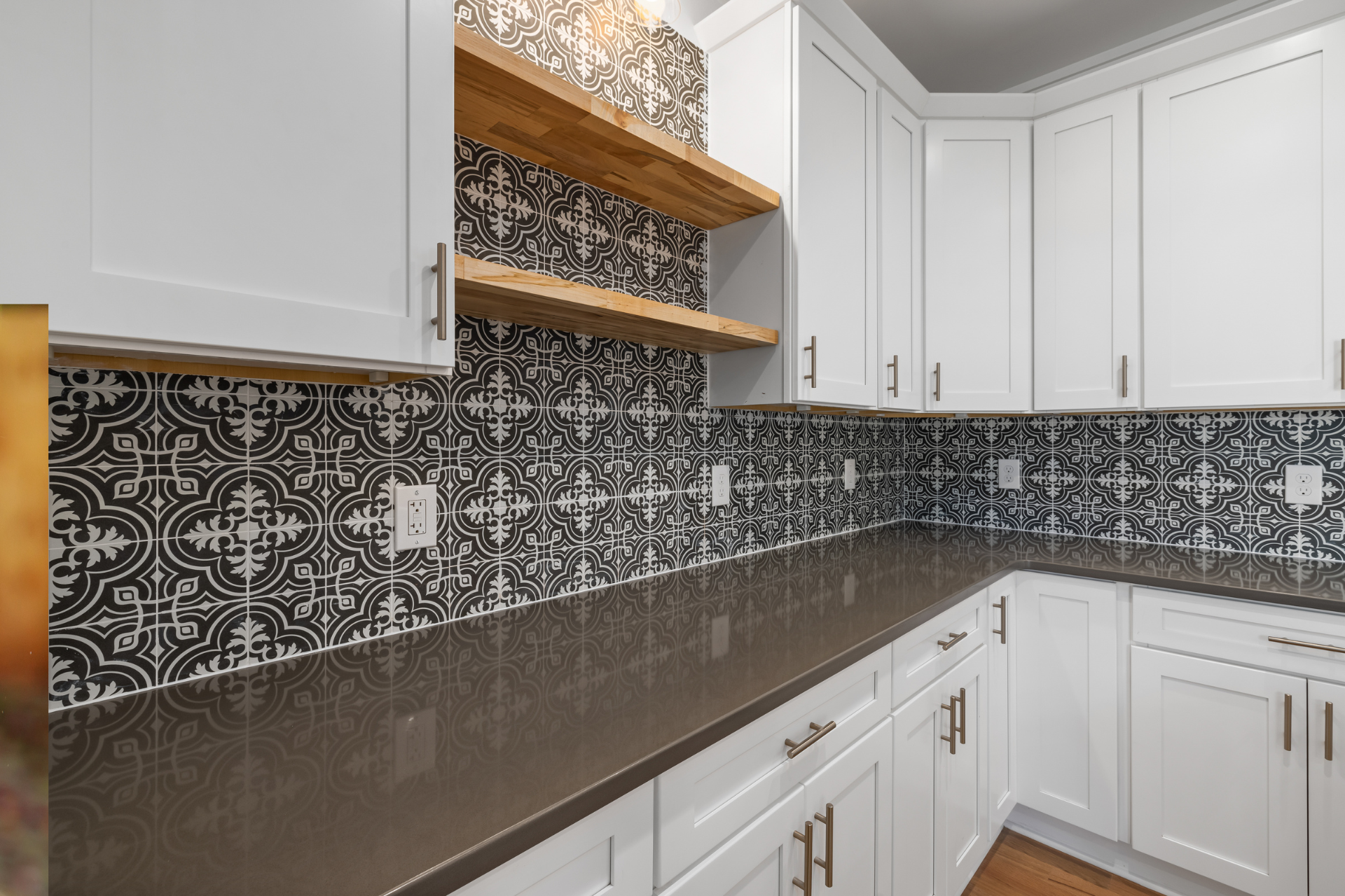 Modern white kitchen with dark patterned backsplash, wood shelves, and black countertops