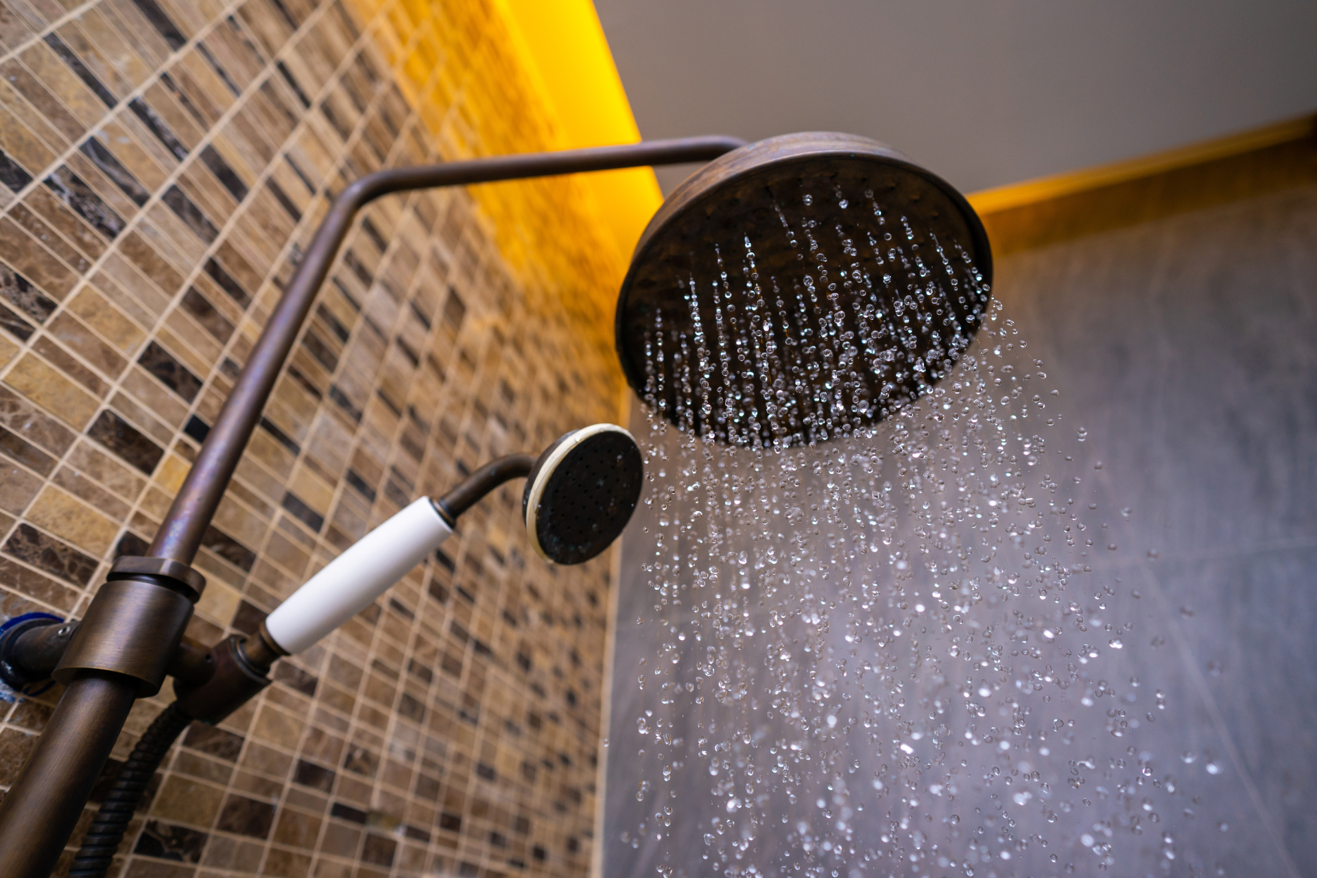 Black rainfall showerhead and handheld shower in a tiled bathroom, water running from the overhead shower