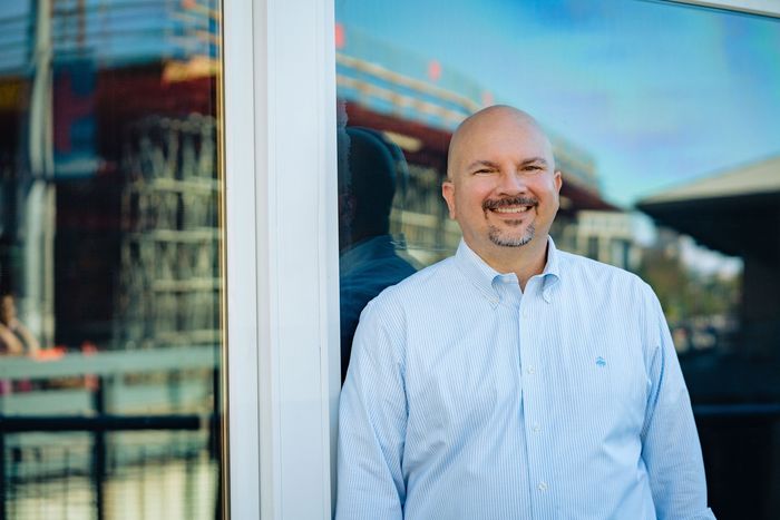H Lee Lewis smiling next to building with reflection of construction