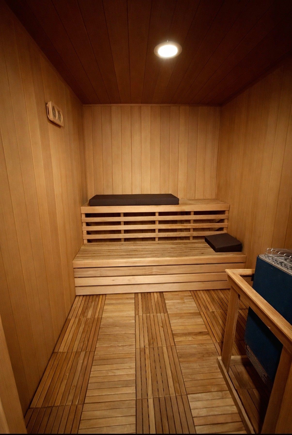 A wooden sauna room with tiered seating benches, a gray seat cushion, and floor duckboards.