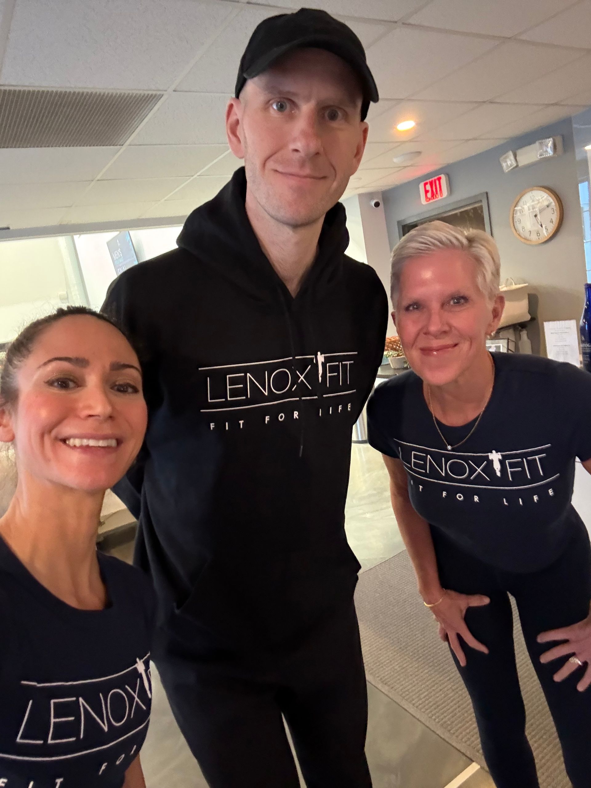 A group of three people wearing matching Lenox Fit gear smile for a selfie in an indoor studio.