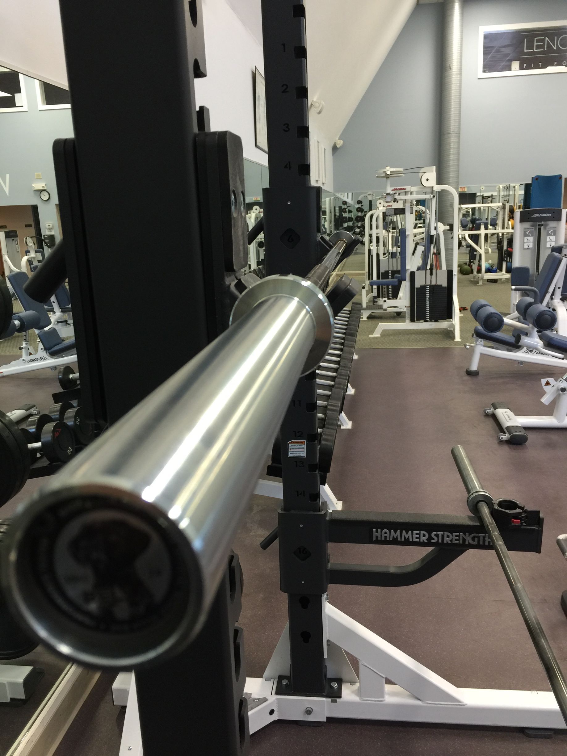 A closeup shot of a chrome barbell resting on a black power rack inside a gym.