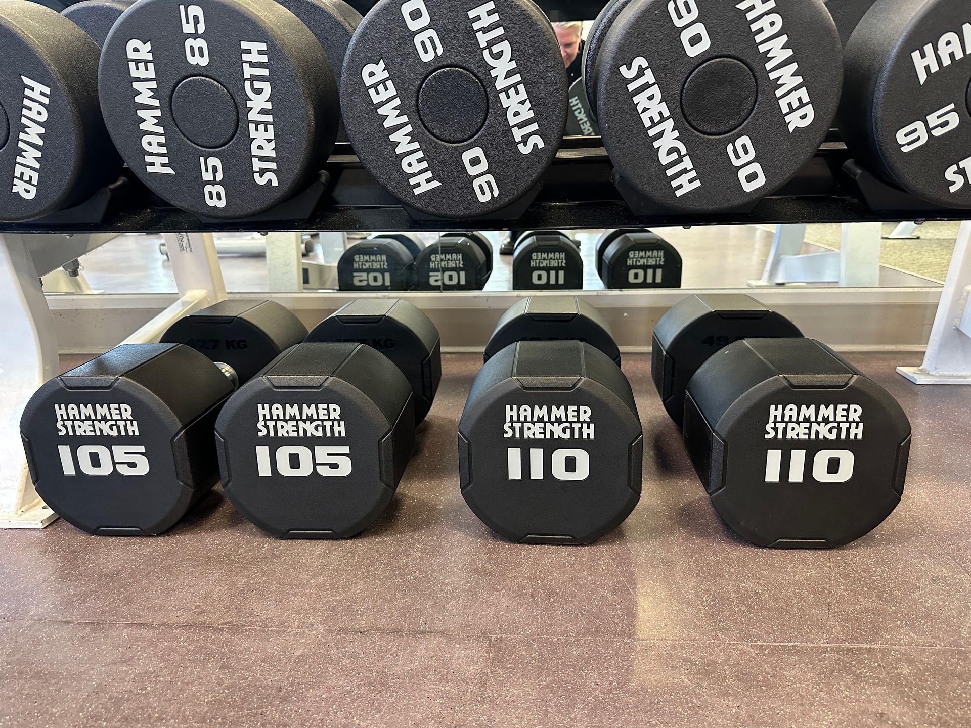 Hammer Strength dumbbells ranging from 85 to 110 pounds arranged on a gym rack.