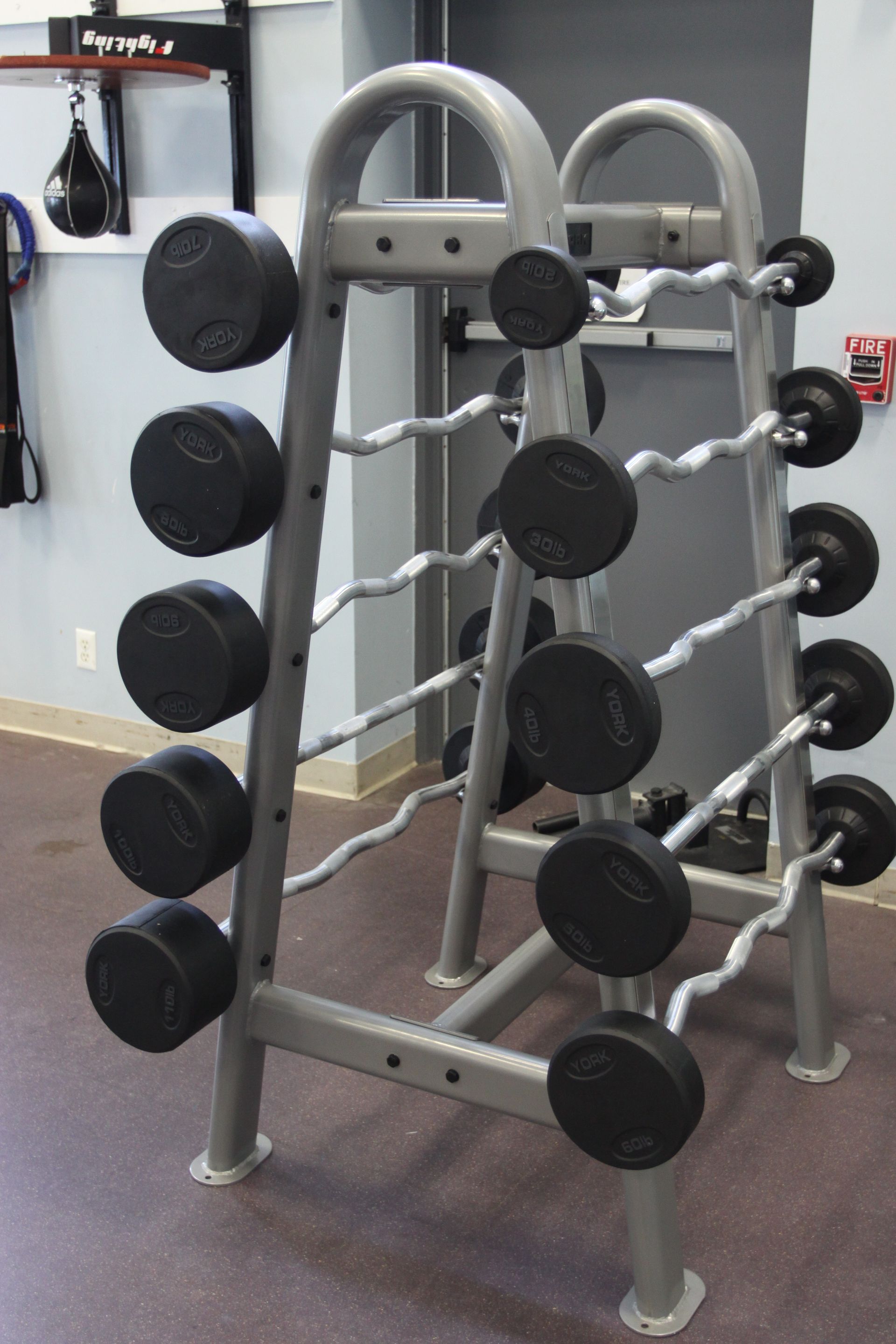 A gray metal weight rack holding several pre-loaded curl bars in a gym.