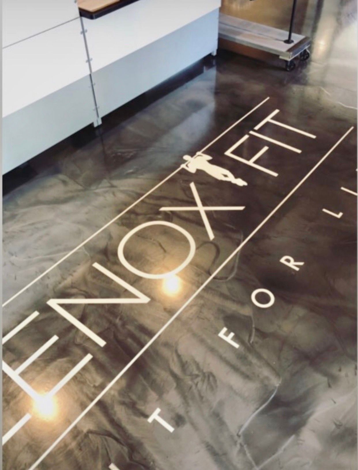 A gym floor with a dark, marbled epoxy finish featuring the white text