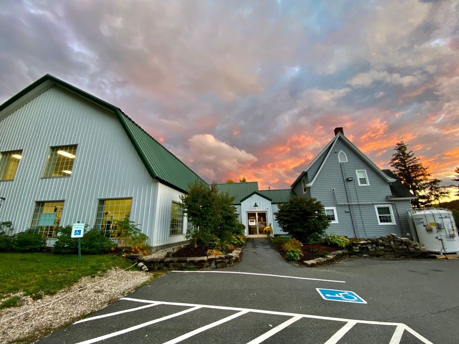 A multi-building complex with a green-roofed white structure and grey siding, under a dramatic sunset sky.