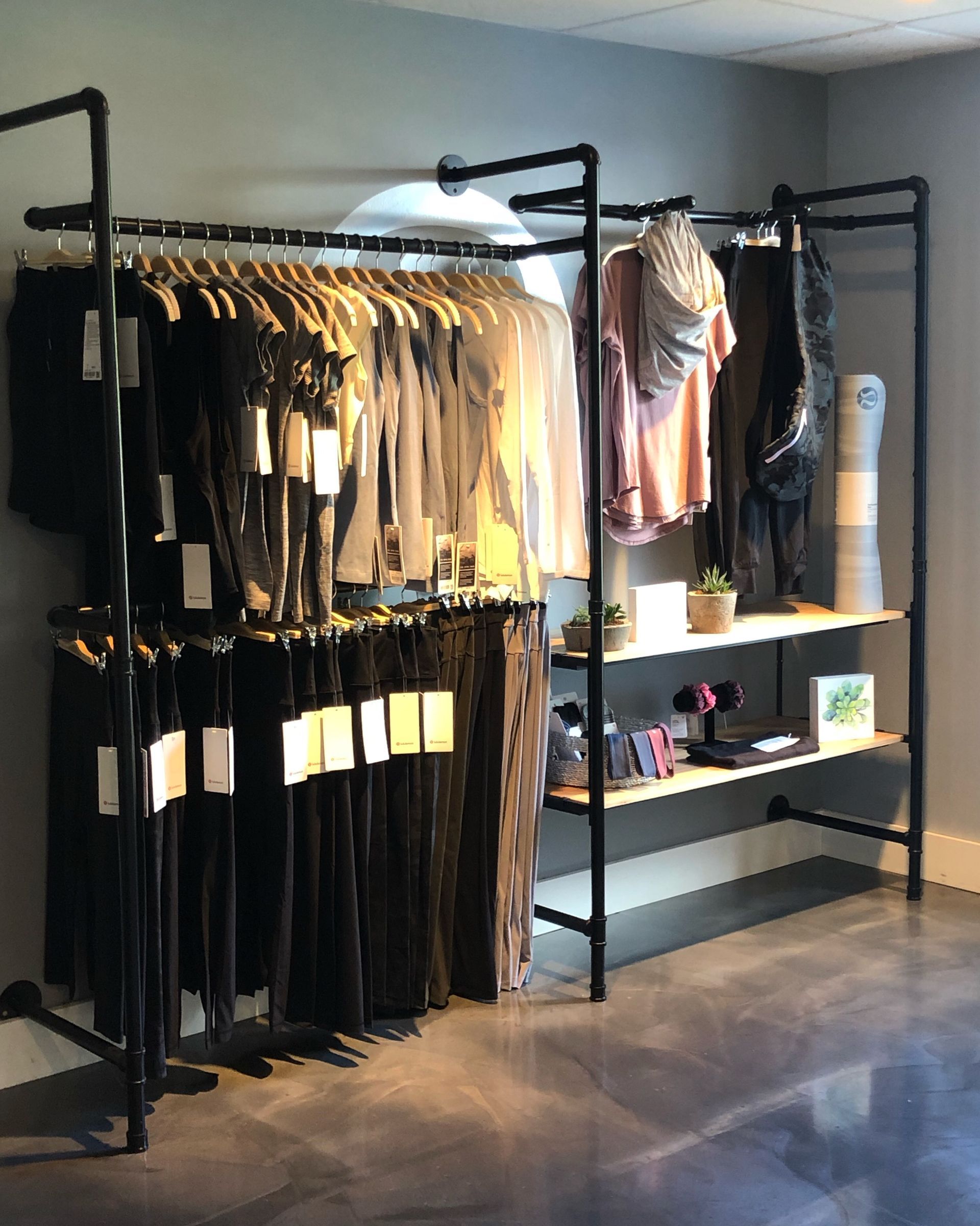 Clothing rack with two levels of hangers, plus shelves displaying folded apparel and accessories against a grey wall.