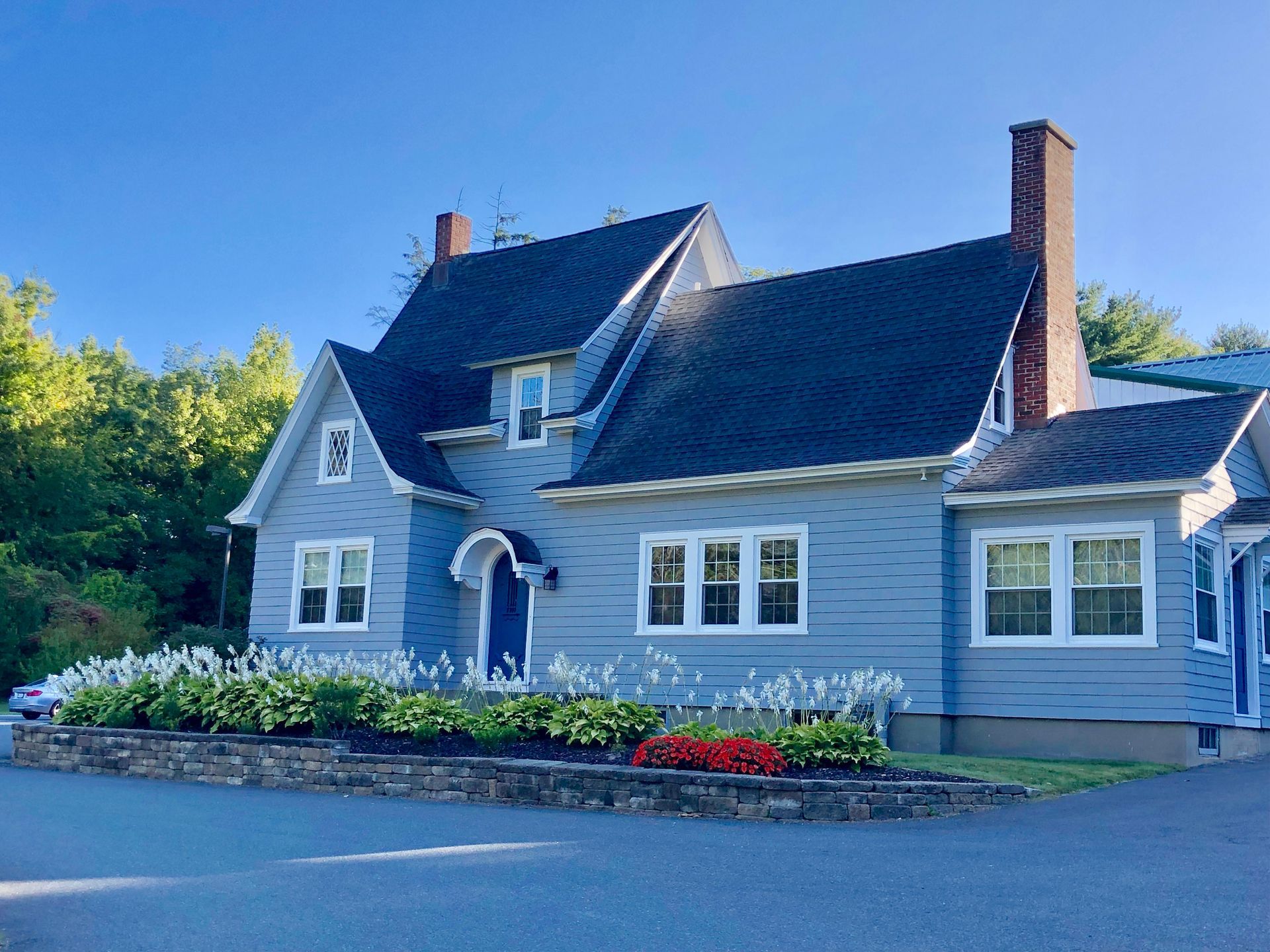 A light blue house with a dark roof and a stone garden border sits under a clear blue sky.