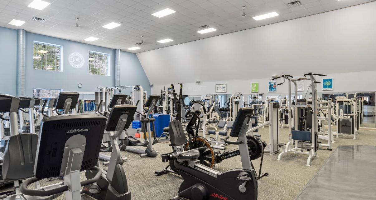 An indoor gym featuring rows of various cardio and strength training equipment under recessed lighting.