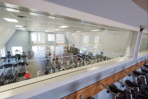 A view from a gym's elevated area looking down through a glass window at exercise equipment and a person sitting below.