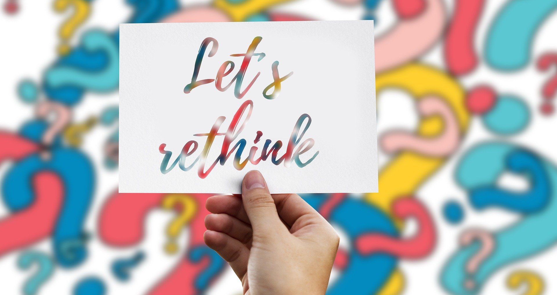 A colorful background of question marks with a hand holding a sign that reads 