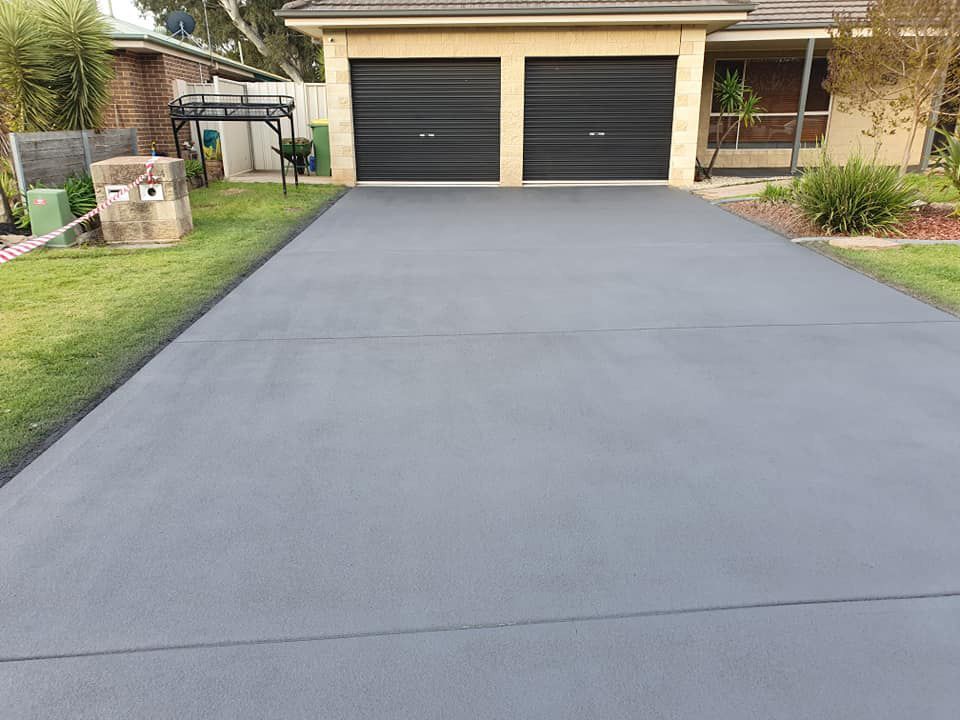 A Concrete Driveway Leading To A House With Two Garage Doors — Custom Concrete Finishes In Thurgoona, NSW