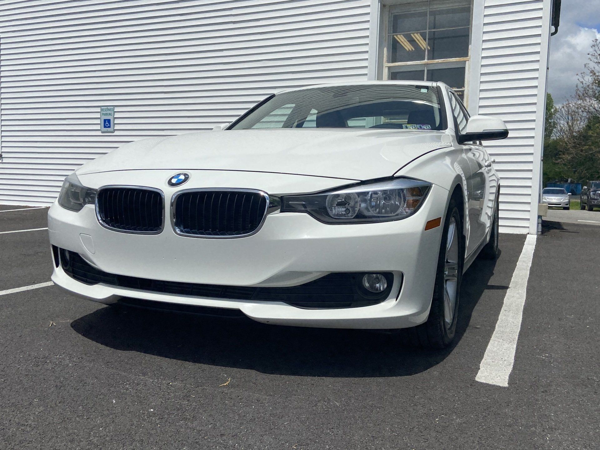 A white bmw is parked in a parking lot in front of a building.