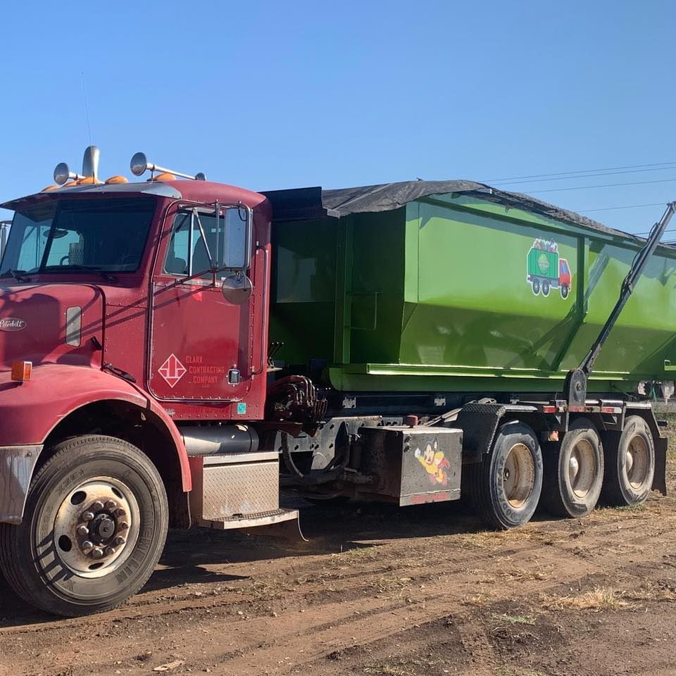 A maroon truck with a lime green dump trailer parked on a dirt lot under a clear blue sky.