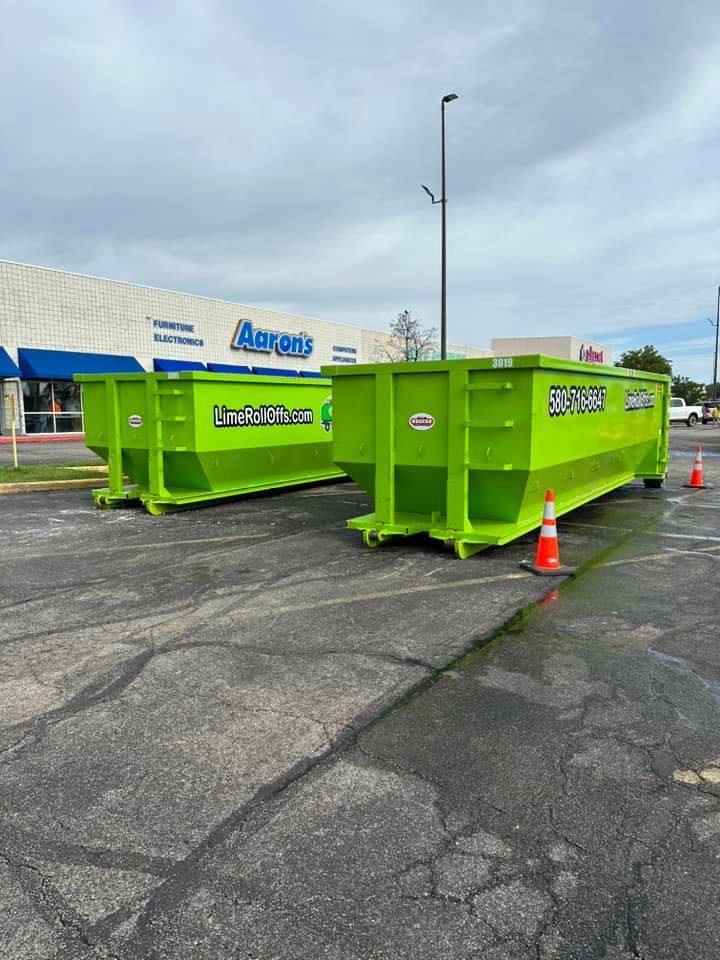 Two lime-green dumpsters sit in a paved lot in front of an Aaron’s store.