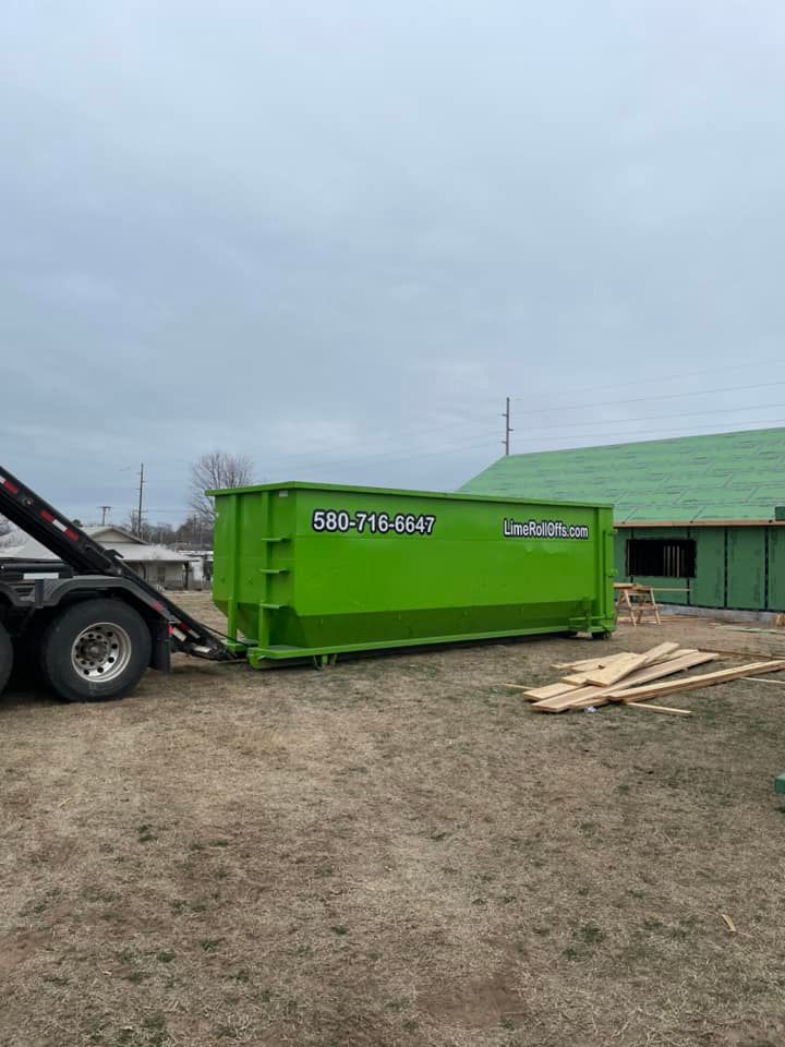 A bright green roll-off dumpster parked on a dirt lot next to a house under construction.