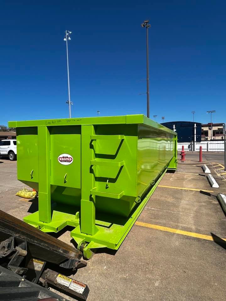 A bright green, empty roll-off dumpster sitting in a paved parking lot on a sunny day.