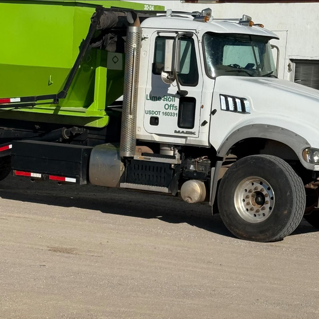 A white commercial dump truck with a bright green container parked on a dirt lot.