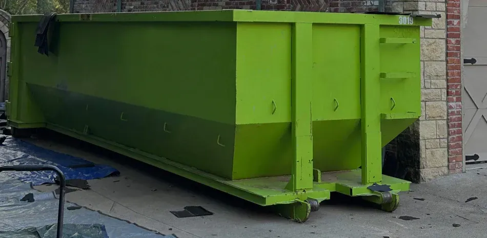 A bright lime-green roll-off dumpster sits on a concrete driveway in front of a brick building.