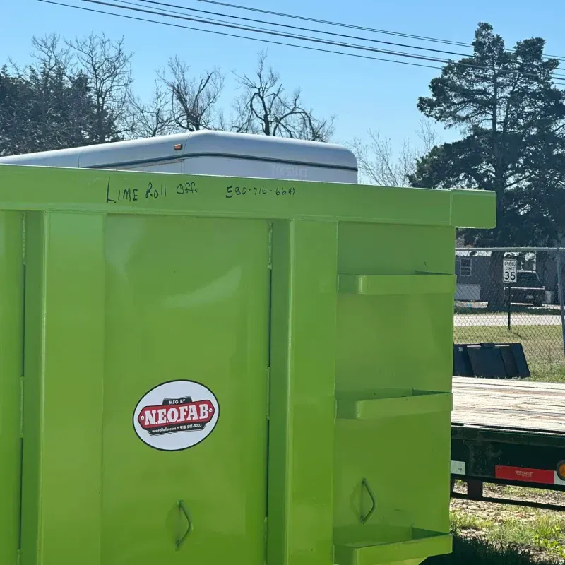 A neon green dumpster by NeoFab featuring handwritten text on its top edge, set against a sunny outdoor background.
