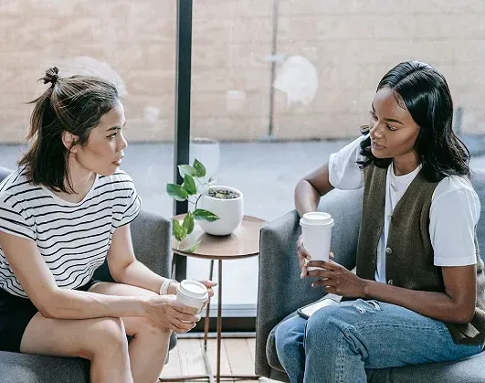 Two women are sitting on a couch talking to each other.