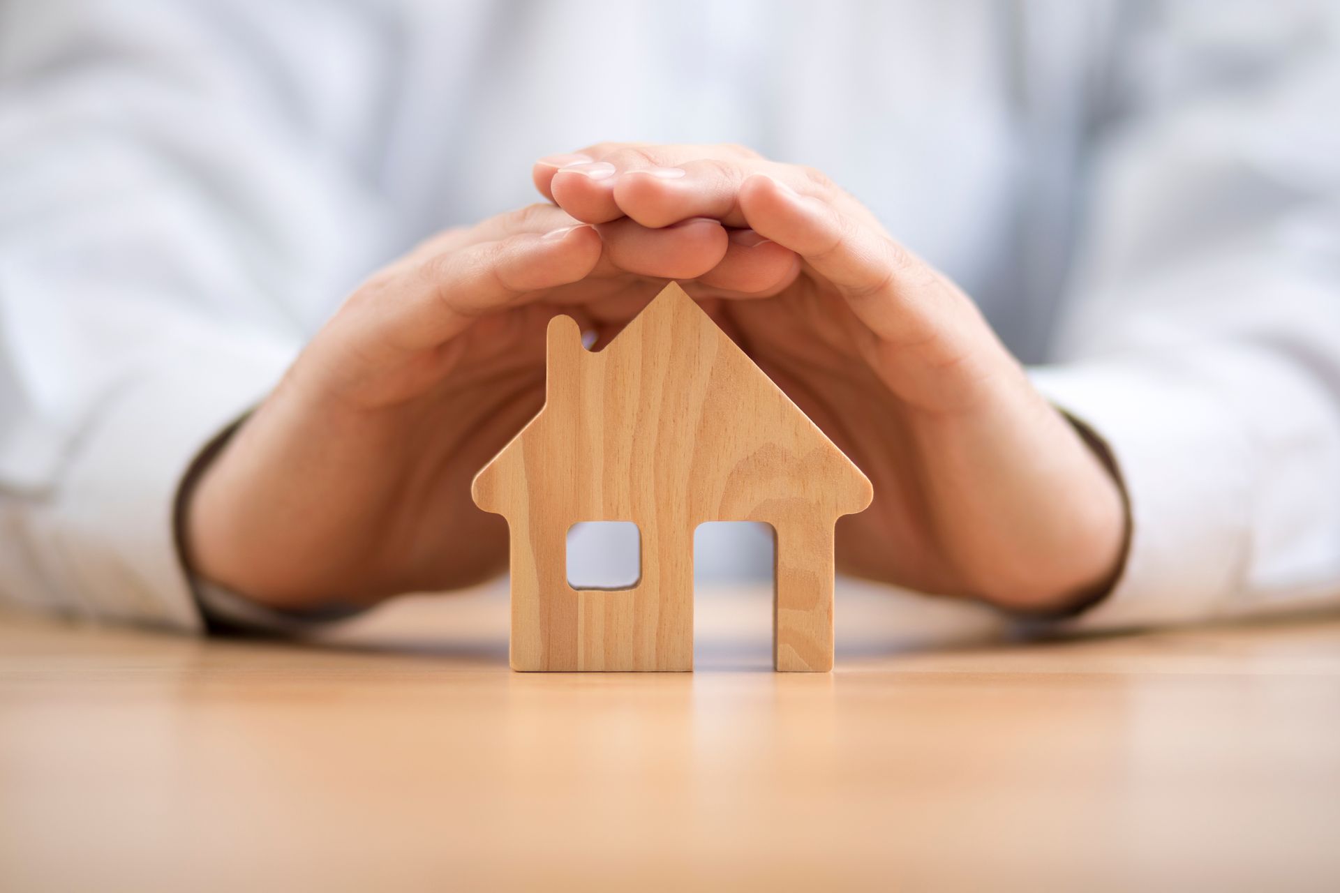 Hands sheltering a wooden house model, representing home insurance