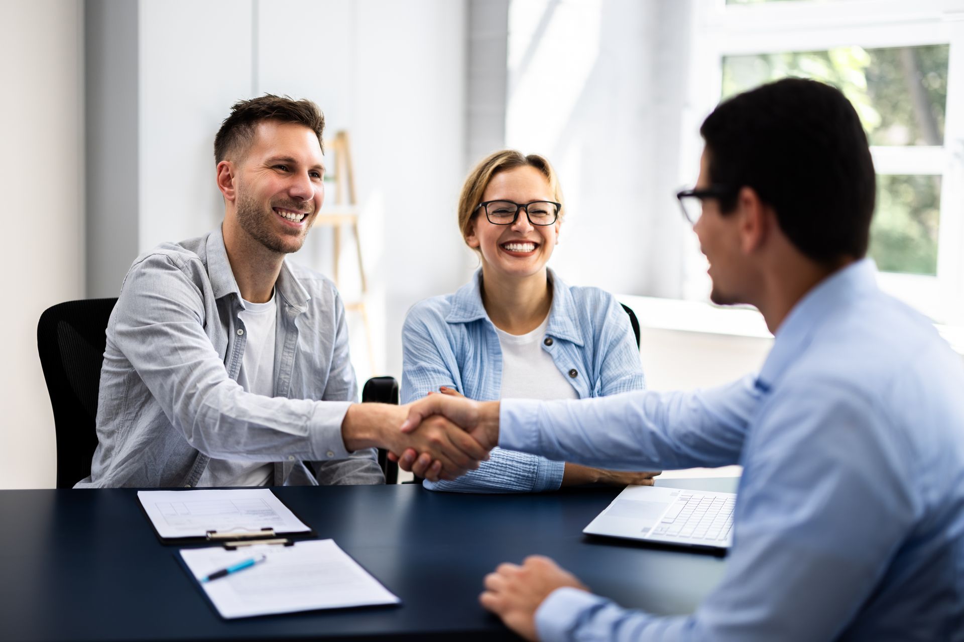 Two clients and an advisor shaking hands across a desk in an office meeting.