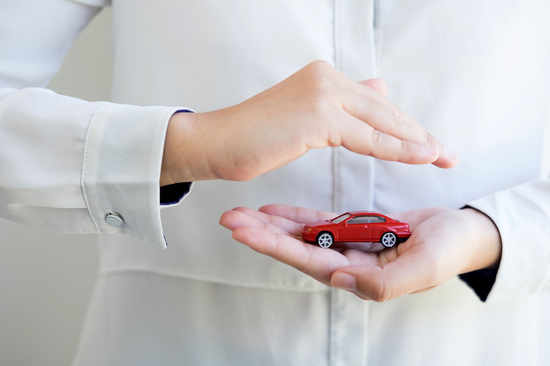 A close-up of a woman holding a red toy car, symbolizing a car insurance agency. A close-up of a woman holding a red toy car, symbolizing a car insurance agency.