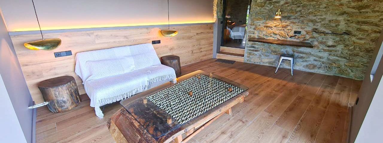 Sala d'estar rústica amb terres de fusta, parets de pedra, sofà i taula de centre. Cal Serni