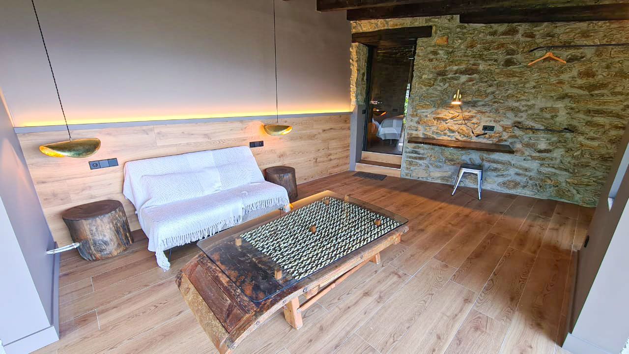 Sala d'estar acollidora amb terres de fusta, paret de pedra i una taula de centre única amb objectes encastats. Cal Serni