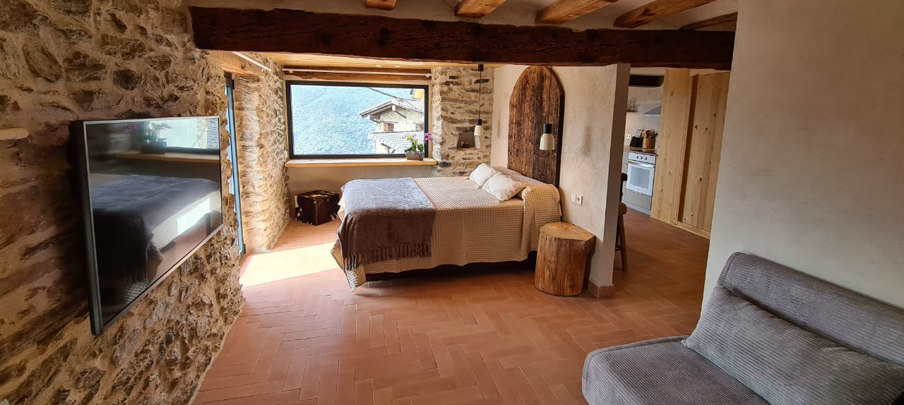 Dormitori amb parets de pedra, un llit amb vistes i un petit sofà. Cal Serni